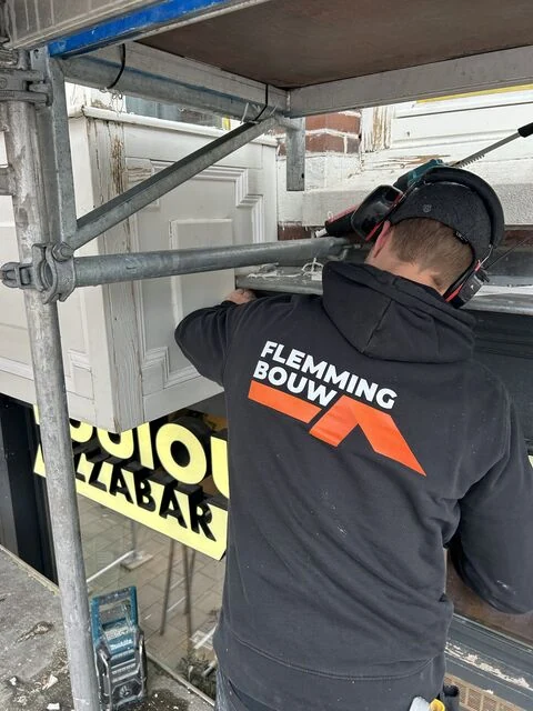 Aan het werk aan een kozijn op de steiger, in Flemming Bouw-werkkleding